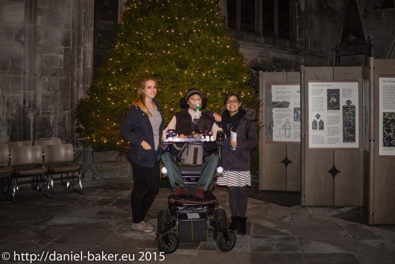 Daniel baker inbetween two women in front of a huge Christmas inside Gloucester Cathedral