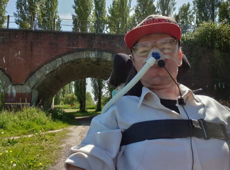 Daniel Baker selfie wearing a red peaked baseball cap sitting under an aqueduct after his wheelchair issues were fixed