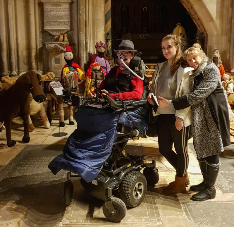 Daniel Baker with his Goddaughter and Mother in front of a knitted nativity scene at Gloucester Cathedral