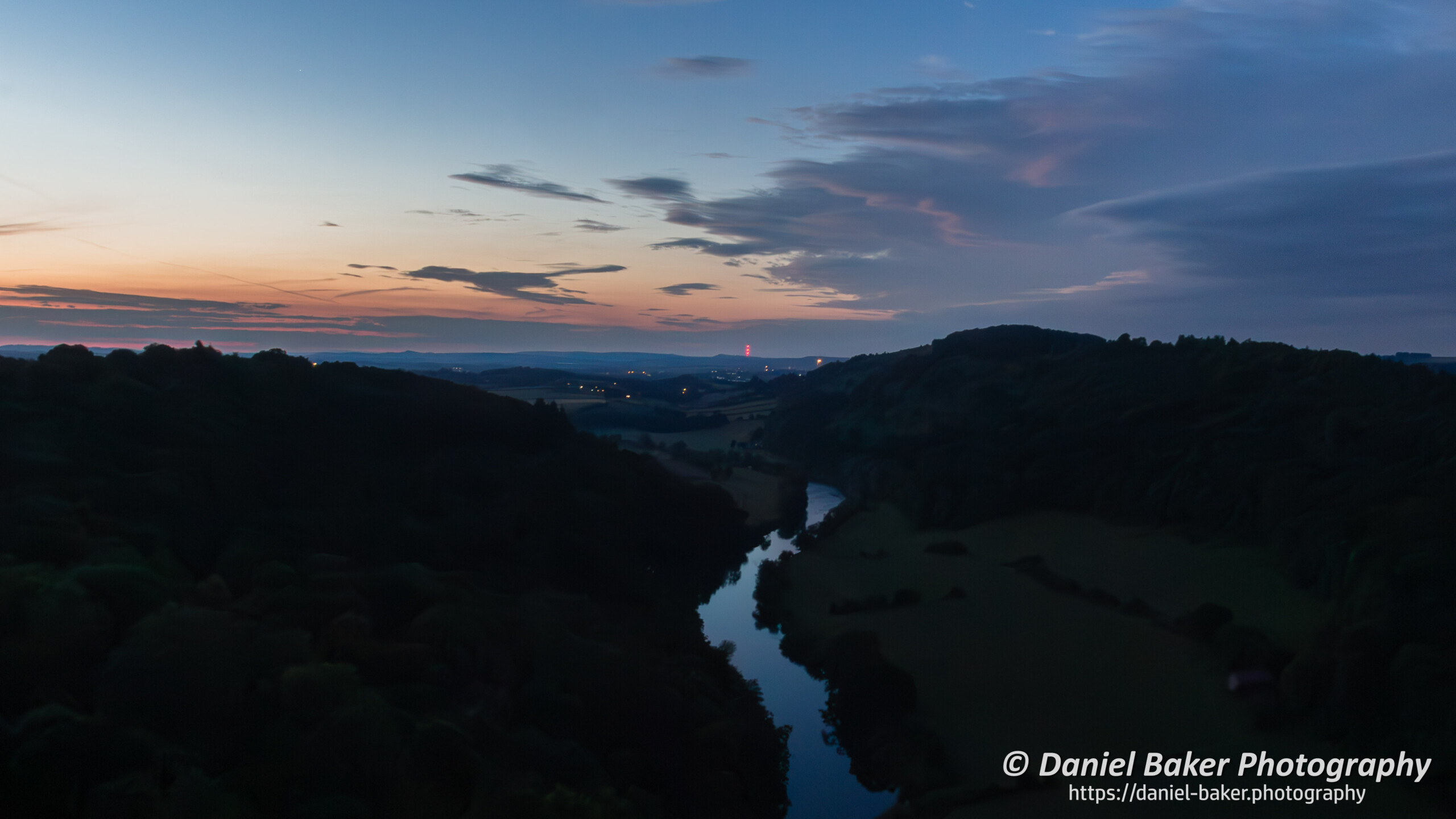 A nighttime view across the Wye Valley just after sunset with orange and blue sky and the river Wye winding into the disastance.